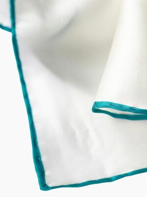 A pair of white pocket squares with teal - colored edges, made of silk.