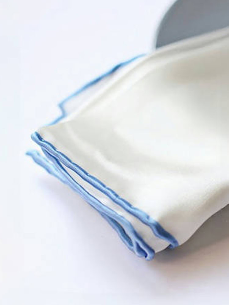 Close - up of a white silk pocket square's hand - rolled ice blue border.