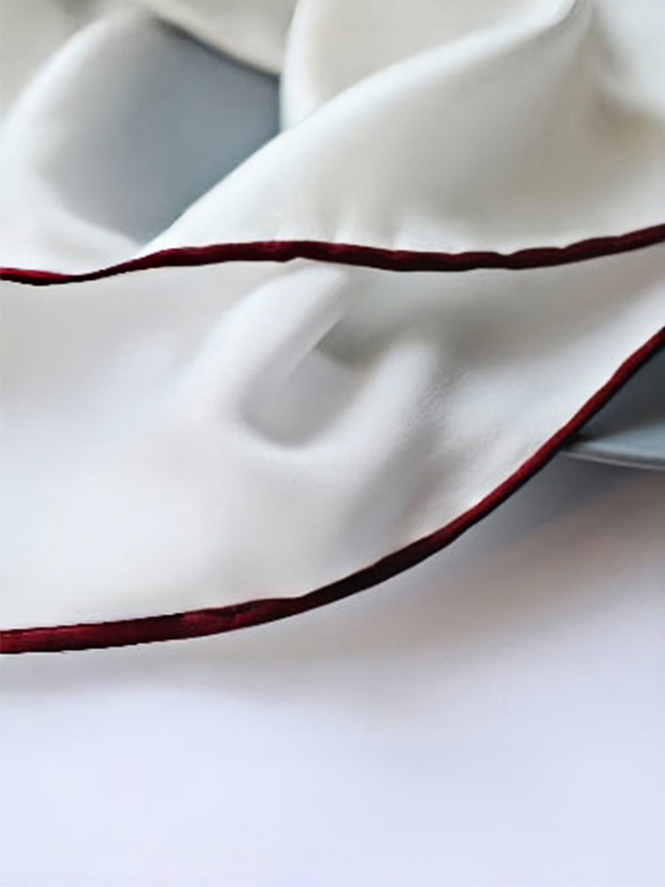 Close - up of a white silk pocket square with a hand - rolled wine - colored border.